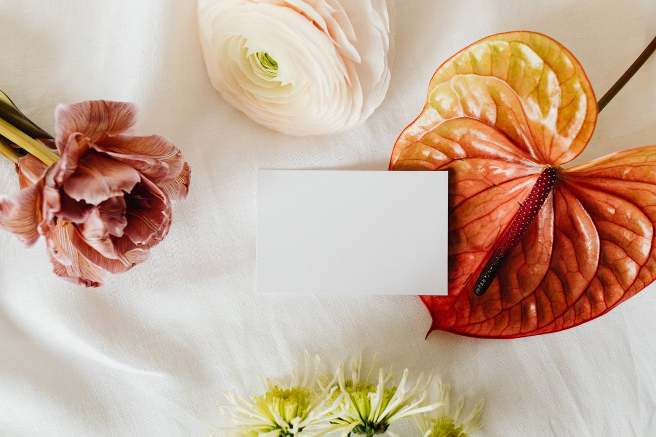 Flat lay of various flowers and a blank card on satin textile backdrop, ideal for invitations.